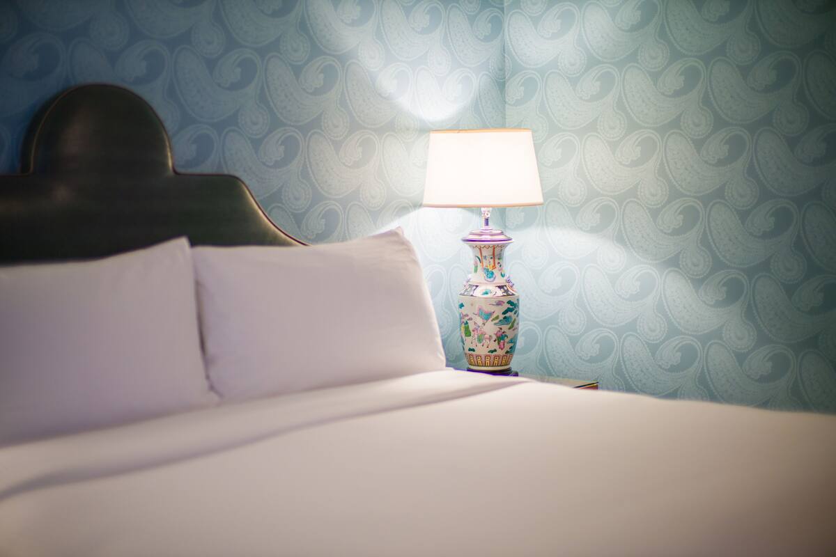 A neatly made bed with white linens and a decorative lamp with a floral design on a nightstand.