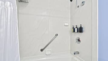 Un baño moderno con ducha, barras de apoyo, dispensador de jabón y perchero para toallas.