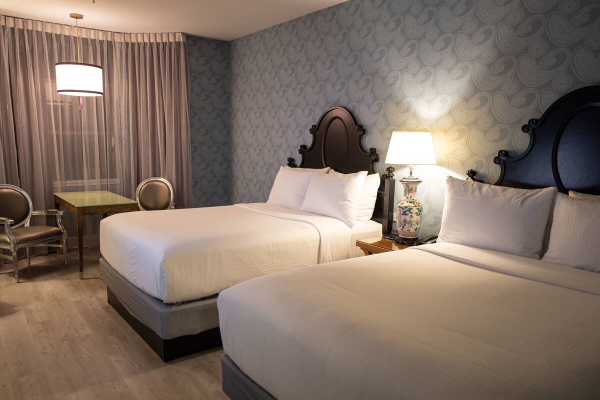 A hotel room with two beds, a desk, and a chair.