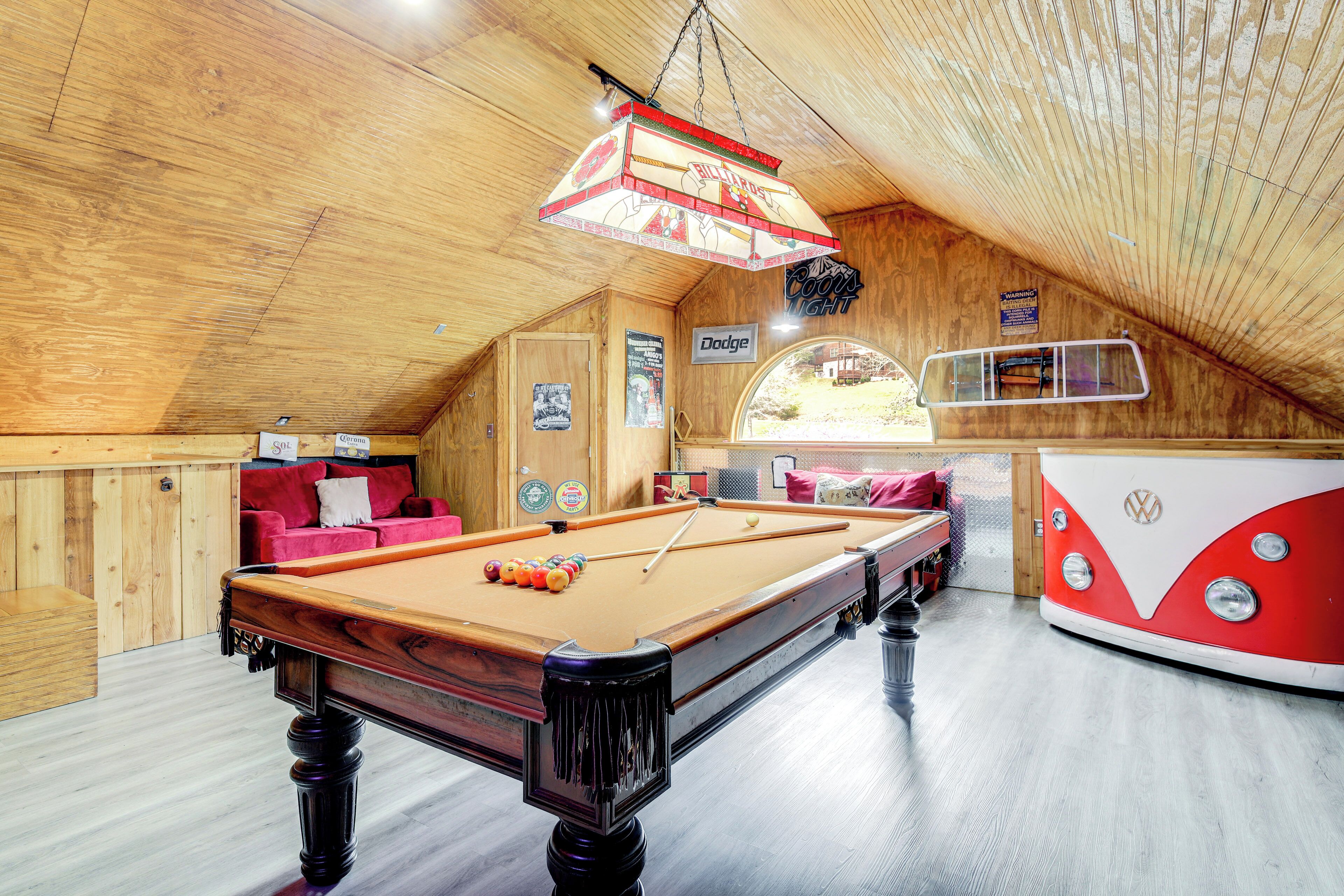 A pool table in a wooden room with a red and white van, a Dodge sign, and a Coors Light sign.