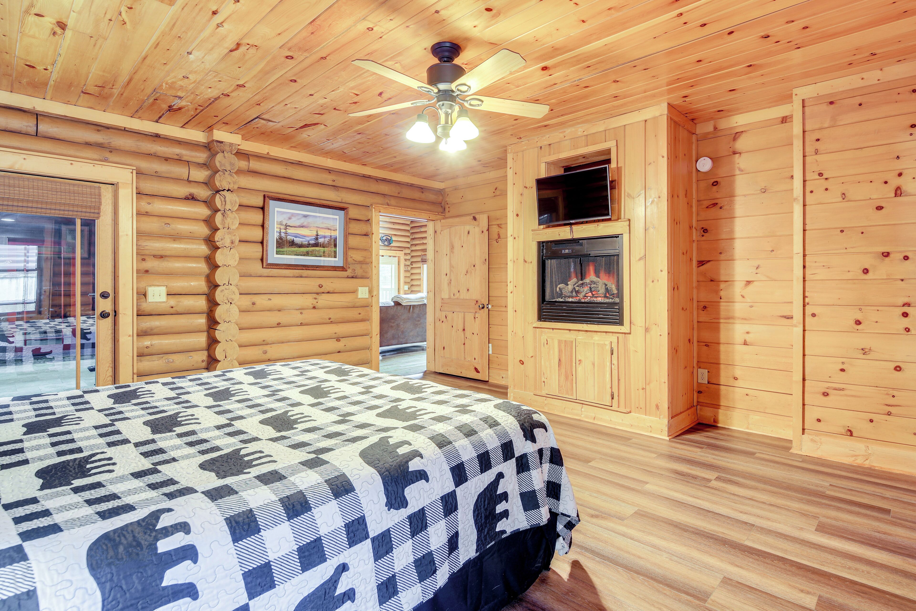 A log cabin room with a bed, a fireplace, a ceiling fan, and wooden walls.