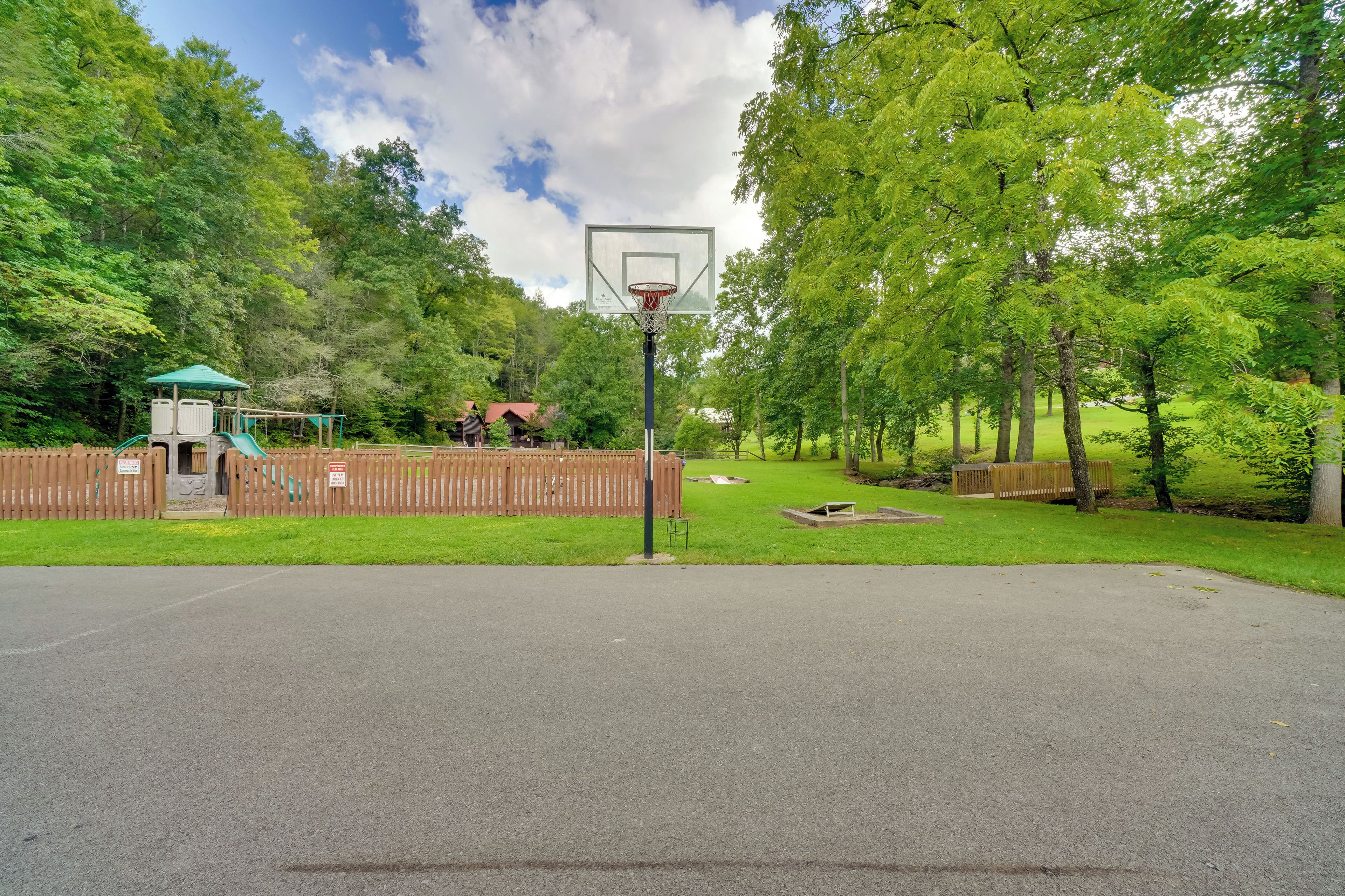 Uma quadra de basquete com cerca de madeira e árvores ao fundo.
