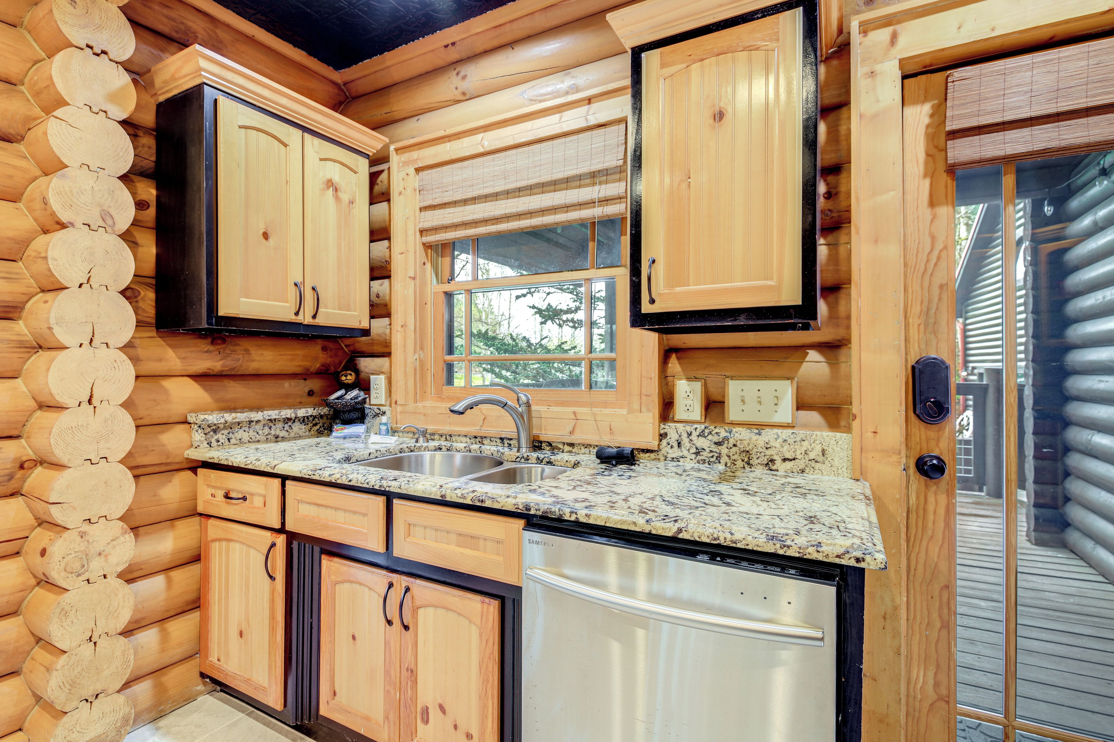Une cuisine rustique aménagée dans une cabane en rondins, avec des meubles en bois, des plans de travail en granit, un évier en acier inoxydable et un lave-vaisselle.