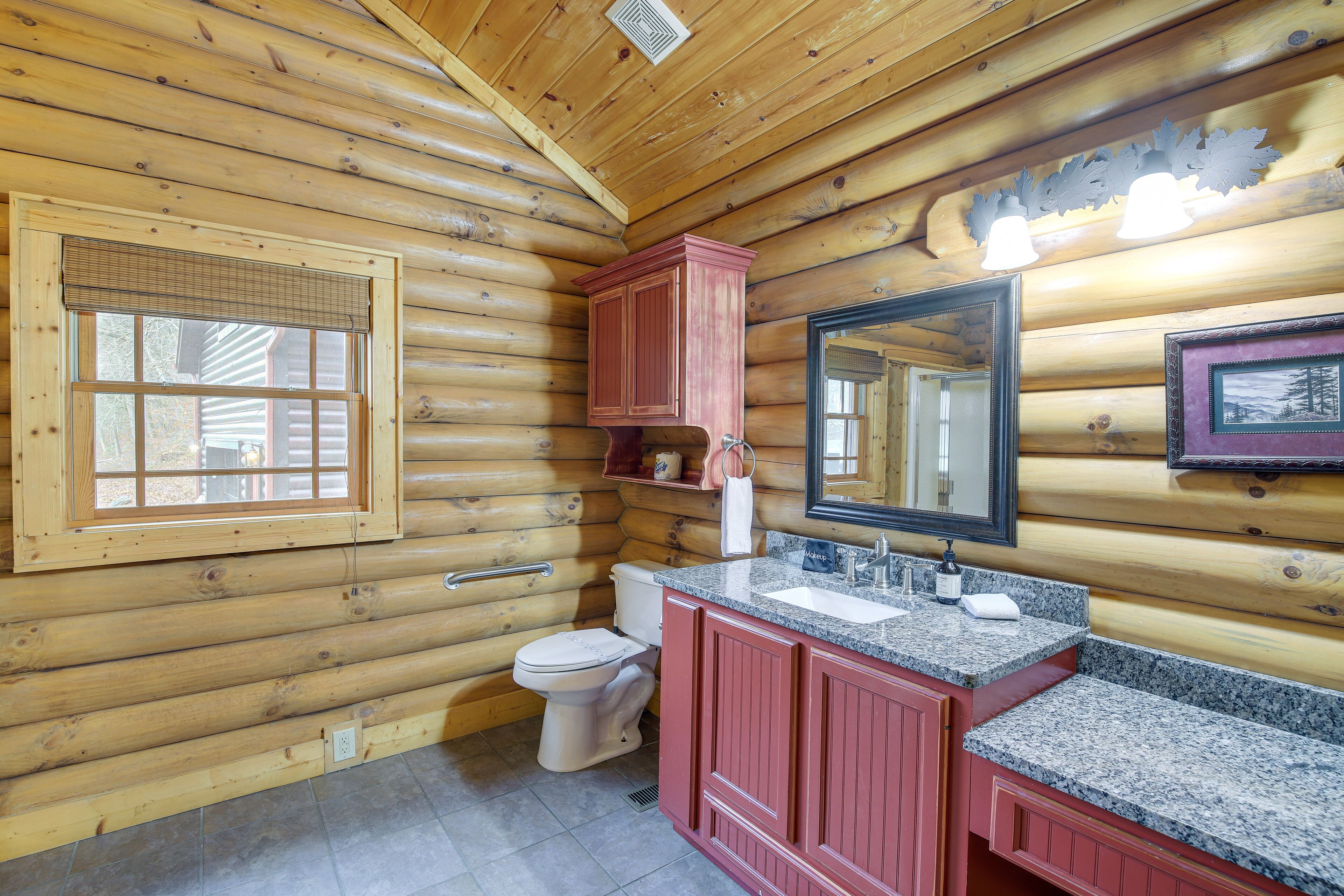 Une salle de bain rustique, aménagée dans une cabane en rondins, avec des toilettes, un lavabo et un miroir.