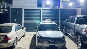 A building with a garage door, a car parked in front, and another car parked beside it. - House 2 Guest House (Lagos)
