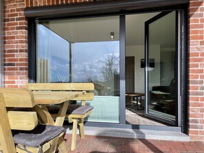 A wooden bench and table outside a building with a glass door. - Tideland 10 - ANKERPLATZ (Westerdeichstrich)