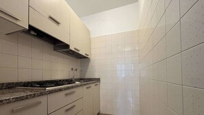 Une cuisine de taille réduite, équipée d’une cuisinière à gaz, d’un évier et de placards.