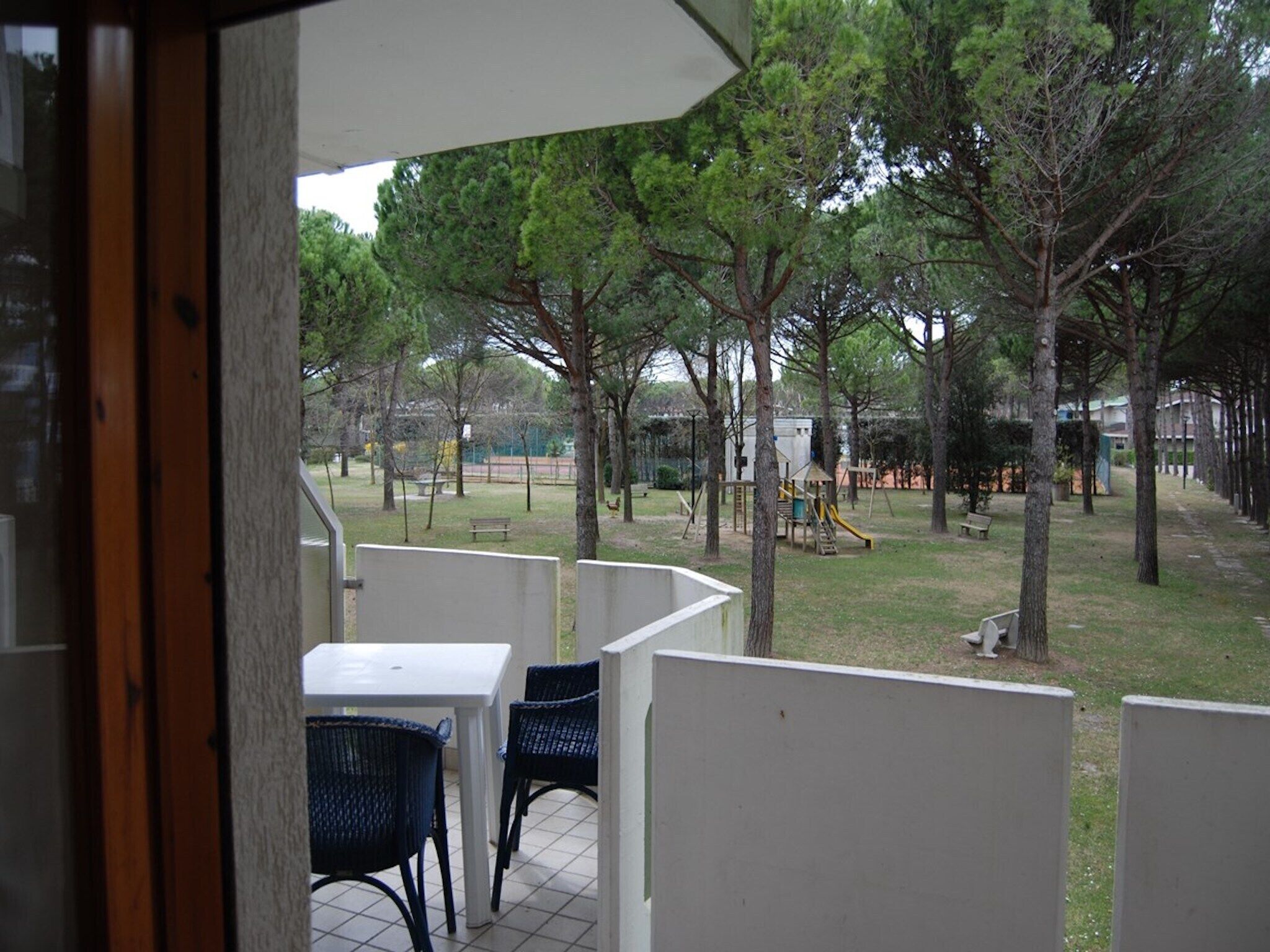 A patio area with a table and chairs, surrounded by trees and a playground in the background.