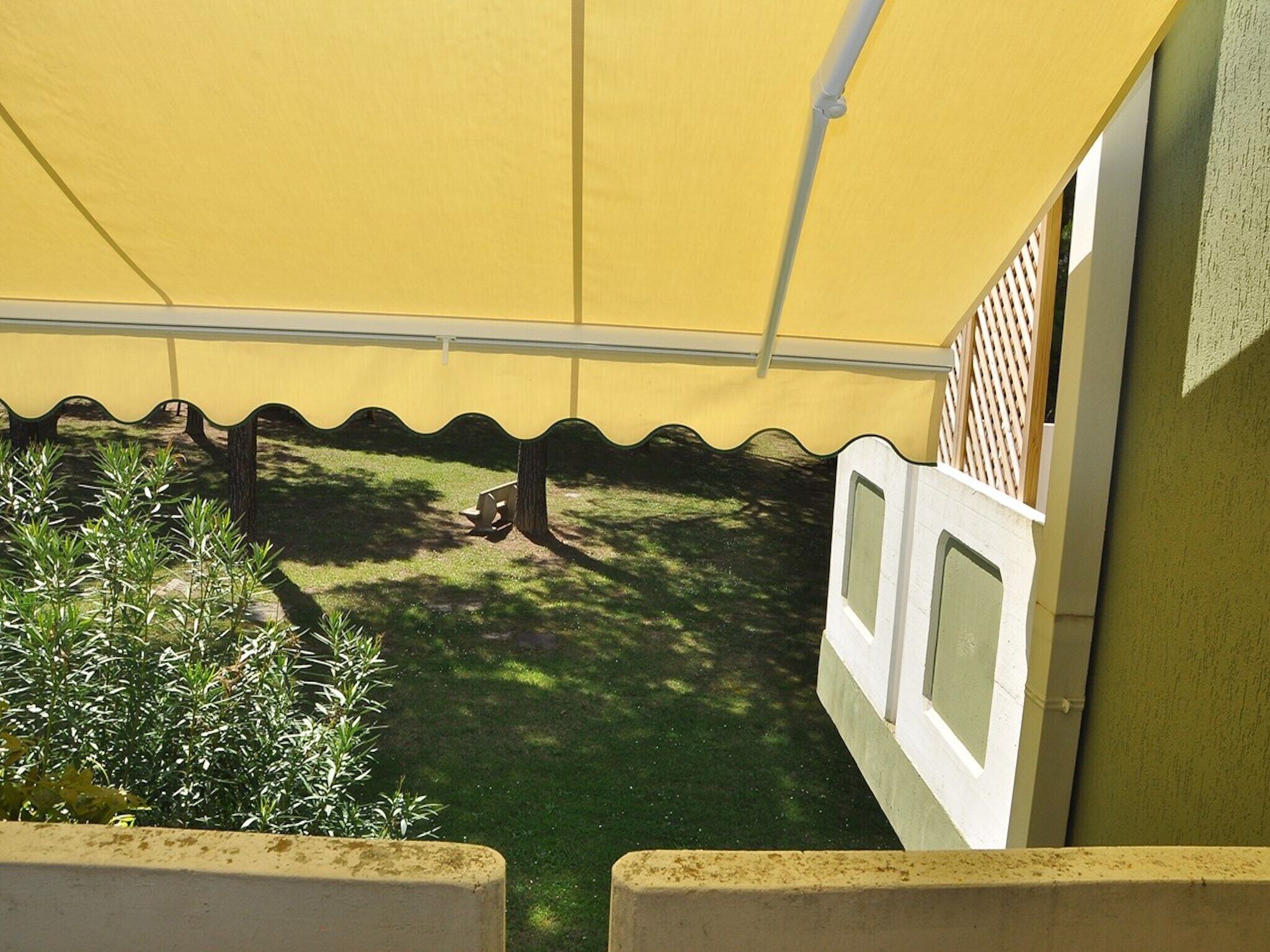 A covered outdoor area with a yellow canopy, a small garden with shrubs, and a white fence.