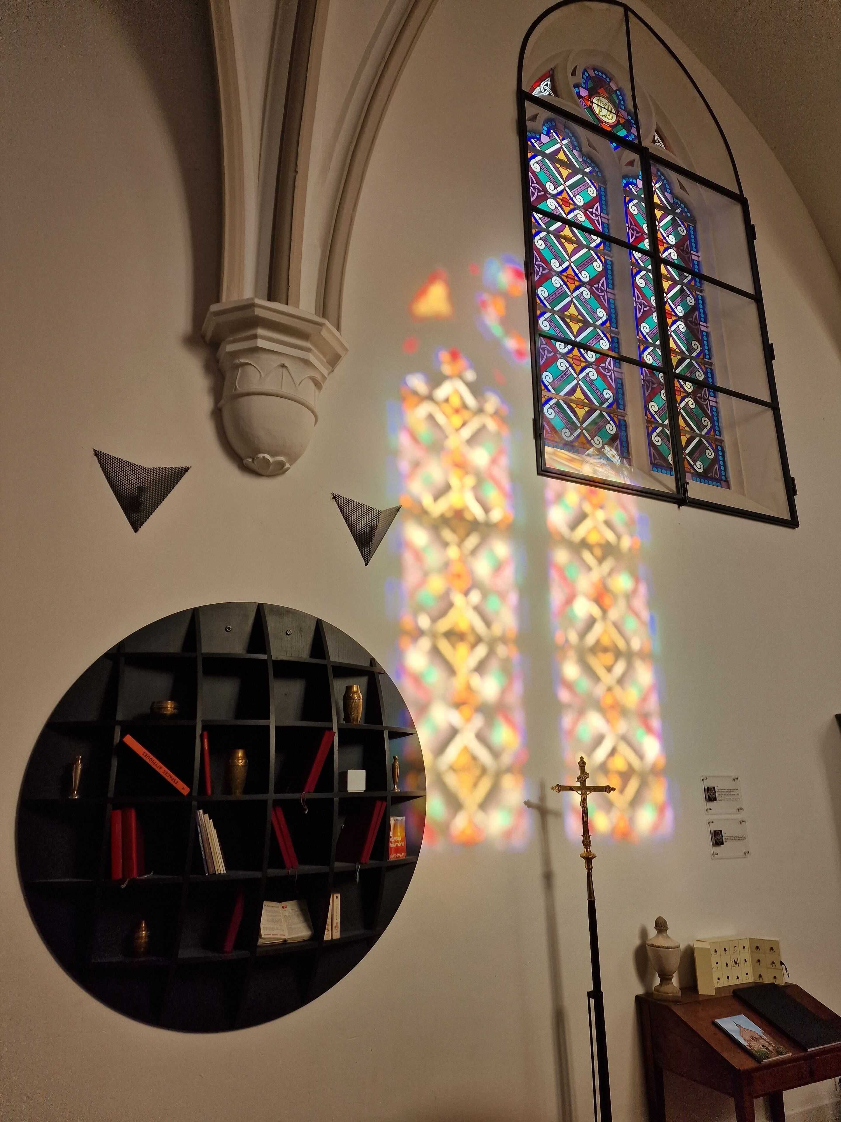 L’intérieur d’une église, avec ses vitraux, une étagère circulaire remplie de livres et un crucifix en bois.