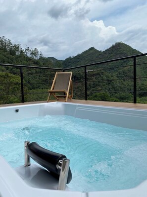 A hot tub on a deck with a view of a forested mountain range.