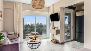 Un salon moderne avec un canapé, une table basse ronde, un téléviseur et un balcon offrant une vue sur la ville.