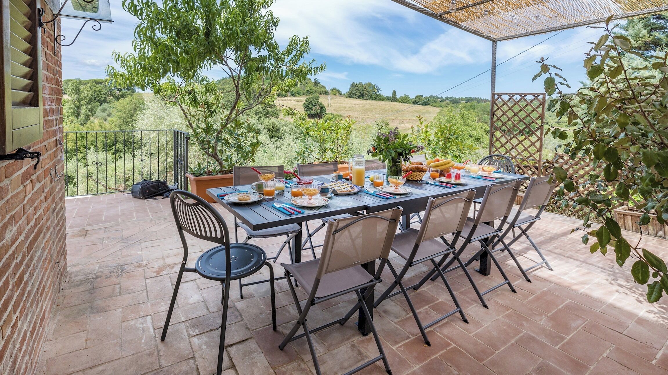 An outdoor patio with a table set for breakfast, surrounded by chairs, and overlooking a scenic landscape.