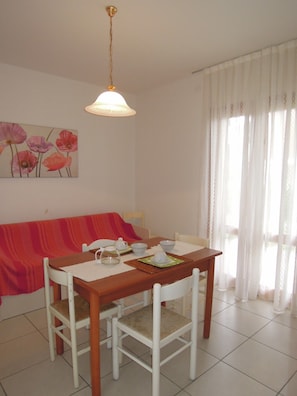 Un coin repas avec une table en bois, des chaises blanches, un canapé rouge et un tableau représentant des fleurs accroché au mur.