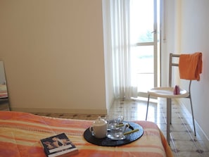 A hotel room with a bed, a chair, a table with a tray of breakfast items, and a window with curtains.