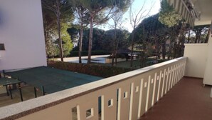 A covered outdoor area with a brick floor, a white building, and trees in the background. - Flat 50m From the Beach (San Michele al Tagliamento)