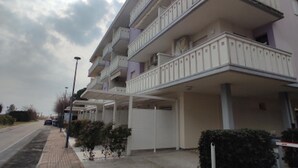 A multi-story residential building with balconies, a paved sidewalk, and a clear sky. - Flat 50m From the Beach (San Michele al Tagliamento)