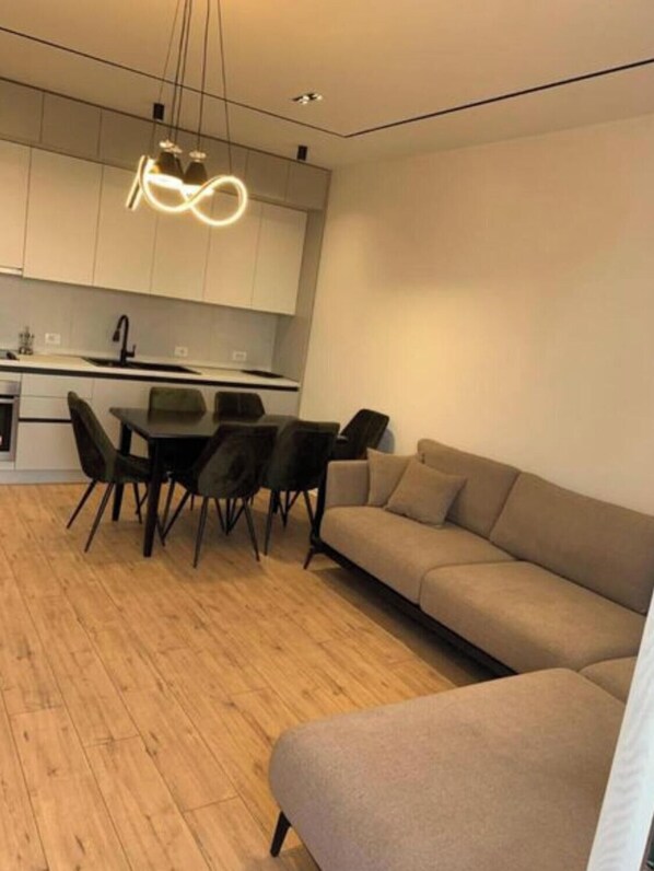 A modern kitchen with a dining area, a sofa, and a wooden floor.
