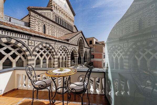 A balcony with two chairs and a table, overlooking a historic building with intricate tile work and arches.