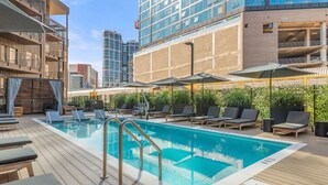 A rooftop pool with lounge chairs and umbrellas, surrounded by high-rise buildings. - ~Walk to Broadway & the Gulch~ King Bed, Balcony, Free Parking, Gym, Pool! (Nashville)