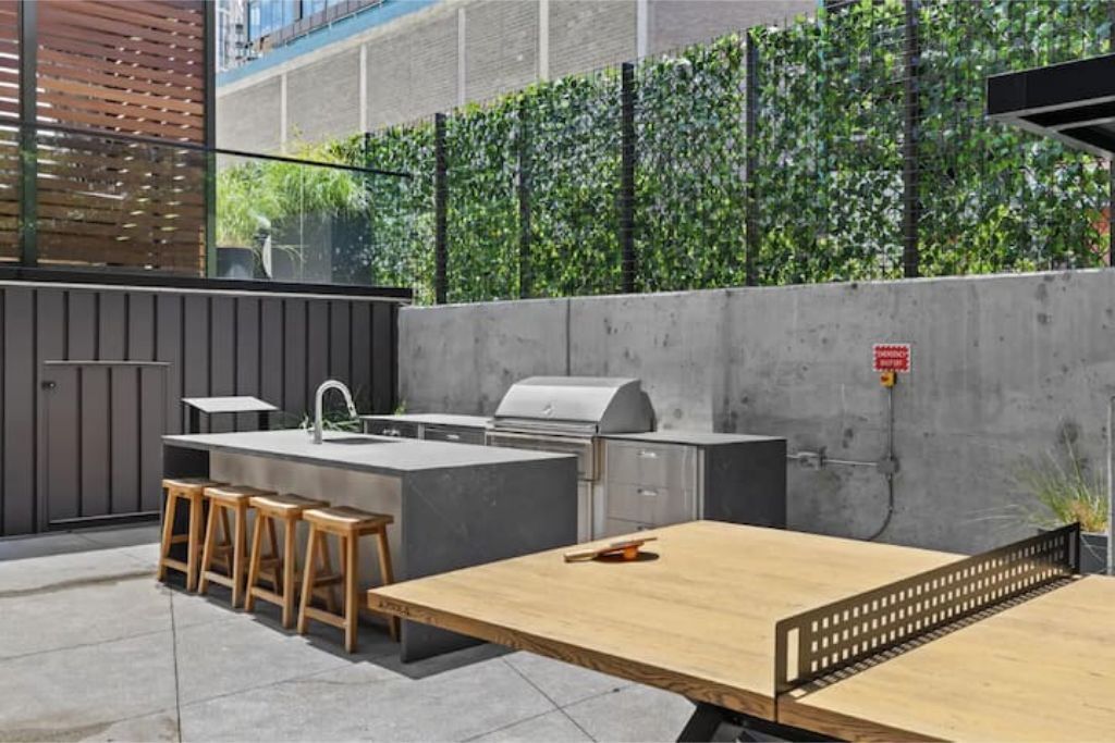 Una cocina al aire libre con una parrilla, taburetes de bar y una mesa de madera.