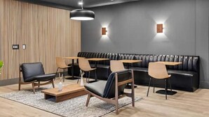 A modern lounge area with a black leather sofa, wooden tables, and chairs. - ~Walk to Broadway & the Gulch~ King Bed, Balcony, Free Parking, Gym, Pool! (Nashville)