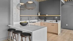 A modern kitchen with a central island, bar stools, pendant lighting, and wooden cabinets. - ~Walk to Broadway & the Gulch~ King Bed, Balcony, Free Parking, Gym, Pool! (Nashville)