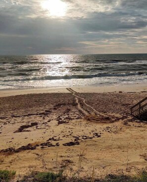 Ein Strand mit einem sandigen Pfad, der zum Wasser führt, einer Holzkonstruktion und einem bewölkten Himmel.