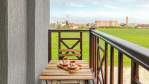 Een balkon met een houten tafel, twee kopjes en een dienblad, met uitzicht op een grasveld en gebouwen.
