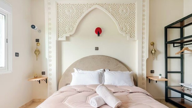 Een slaapkamer met een groot bed, decoratieve plafondaankleding, wandplanken en een hangende kledingrek.