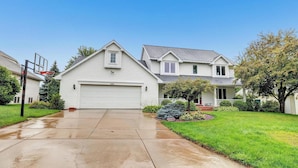 A two-story house with a garage, a basketball hoop, and a well-maintained lawn.