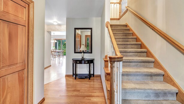 A hallway with wooden flooring, a black console table, a mirror, and a carpeted staircase with wooden railings.