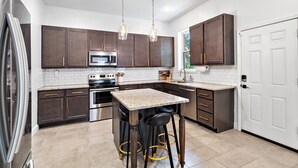 Una cocina moderna con armarios de madera oscura, electrodomésticos de acero inoxidable, encimera de granito y una zona con taburetes de bar.