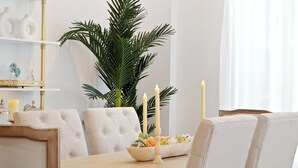 Un comedor con una mesa de madera, sillas blancas tapizadas, una planta en maceta y velas.