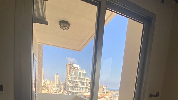 Un balcón con vista a la ciudad, una puerta corrediza de vidrio y piso de baldosas.