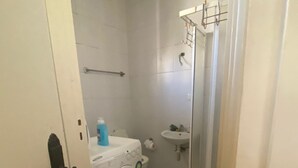 Un baño pequeño y funcional con lavadora, lavamanos y zona de ducha.