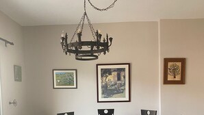 Un comedor con una mesa redonda, seis sillas, una araña y tres cuadros en la pared.