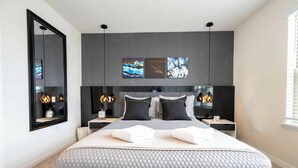 A modern bedroom with a large bed, two bedside tables, a mirror, and artwork on the wall. - Amazing Home at Windsor Westside (Kissimmee)