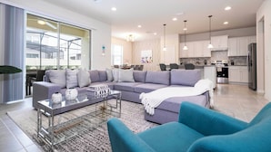 A modern living room with a sectional sofa, a glass coffee table, and a blue armchair. - Amazing Home at Windsor Westside (Kissimmee)