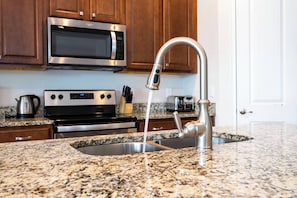 Cozinha com bancadas de granito, eletrodomésticos de aço inoxidável e armários de madeira.