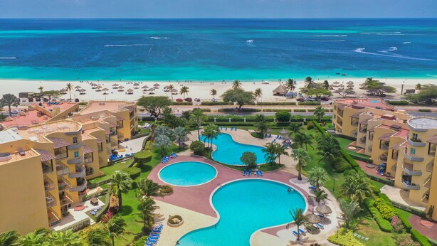 A resort with two large swimming pools, a beach, and a view of the ocean.
