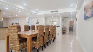 A dining area with a wooden table and wicker chairs, a kitchen in the background, and a hallway leading to other rooms.