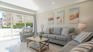 A modern living room with a grey sofa, a wooden coffee table, and a glass door leading to an outdoor area.