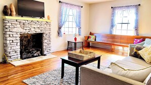 Una sala de estar con chimenea de piedra, televisor de pantalla plana, sofá, banco y mesa de centro.