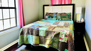 Un dormitorio con una cama, una ventana con cortinas, una lámpara de noche y una mesita de noche.