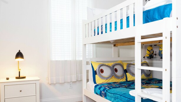 A bunk bed with a Minion-themed bedspread, a white nightstand with a lamp, and a window with blinds. - Beautiful Townhome W/pool Close to Disney (Davenport)