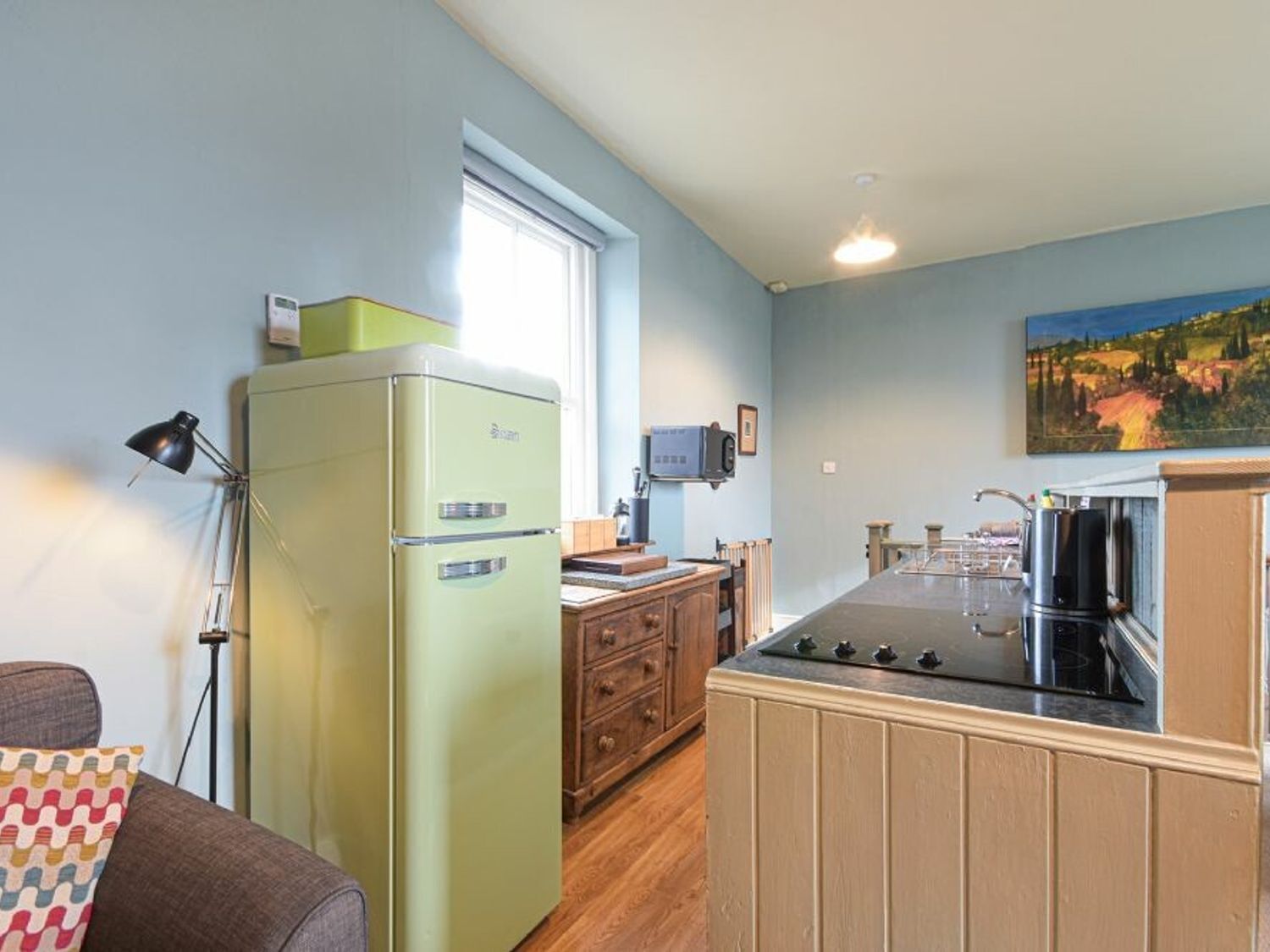 A compact kitchen with a vintage refrigerator, wooden cabinets, a stove, and a window providing natural light.
