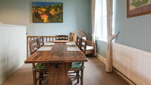 A dining room with a wooden table and chairs, a painting on the wall, and a window with curtains.
