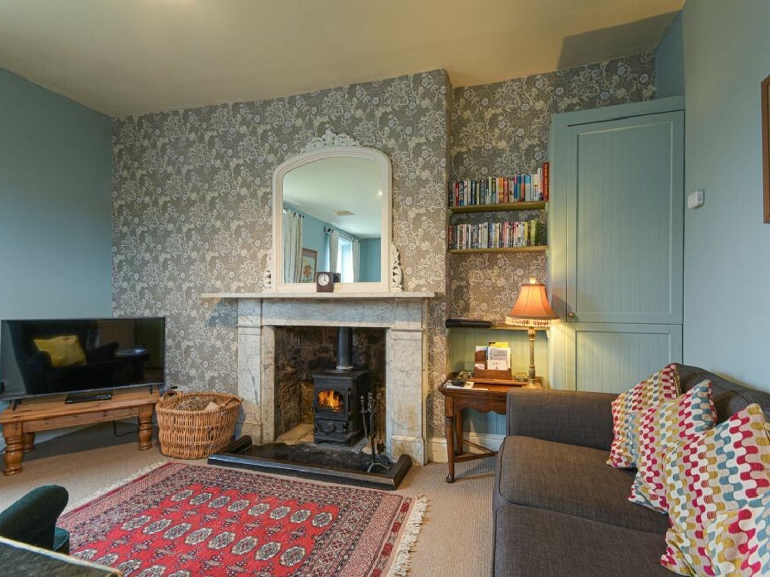 Un salon chaleureux avec une cheminée, un téléviseur, une bibliothèque et un tapis à motifs.