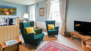 A living room with two green armchairs, a television, a coffee machine, and a painting on the wall.